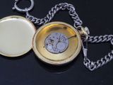 a gold pocket watch with a chain on a black surface