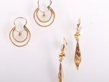 trois paires de boucles d'oreilles en or et une boucle d'oreille en perle posées sur un fond blanc