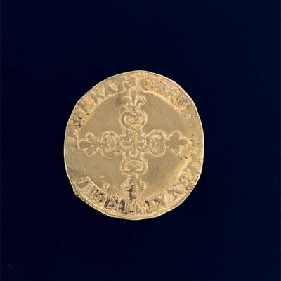 une vieille pièce d'or sur laquelle figure une croix, sur fond noir