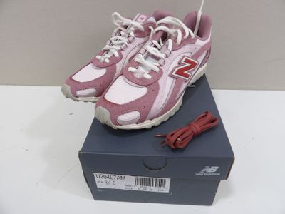 des chaussures New Balance roses avec des lacets blancs, posées sur une boîte