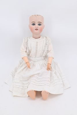 an old doll sitting on a white surface wearing a white dress