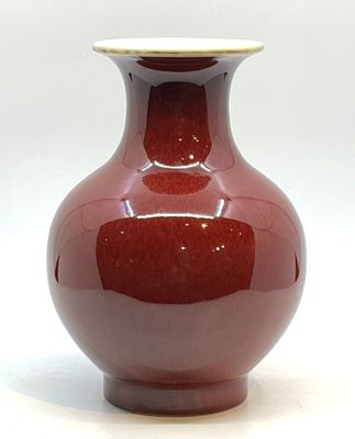 un vase rouge posé sur une table, sur fond blanc