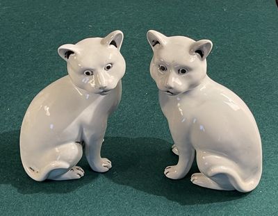 two white ceramic cats sitting next to each other on a green surface