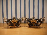 pair of black and gold teapots on wooden table with blue and white striped wallpaper