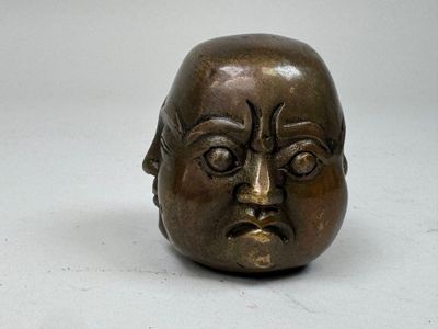 une petite sculpture en bronze représentant un visage sur une surface blanche