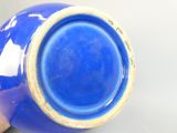a blue vase sitting on a table with a hand holding it
