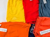 six pairs of colorful pants are laid out on a bed