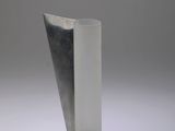 un vase argenté posé sur une surface blanche, avec un fond gris