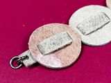two silver and gold coin charms on a pink surface