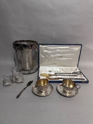 deux tasses et soucoupes en métal argenté, présentées dans une boîte avec une cuillère et un couteau
