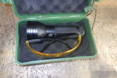 une mallette verte posée par terre, contenant une lampe de poche