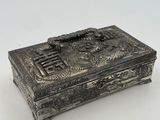 an old silver box with a dragon on it sitting on a white surface