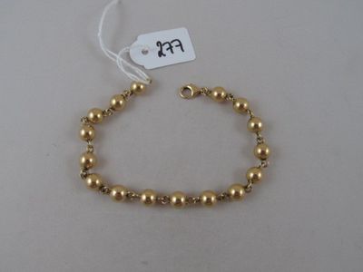 a close up of a gold beaded bracelet on a white surface