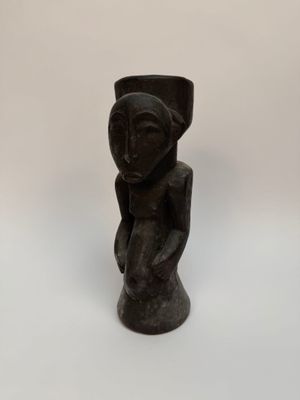 une sculpture noire représentant une femme tenant un vase posé sur une table