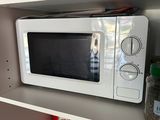 a white microwave on a shelf with a roll of toilet paper