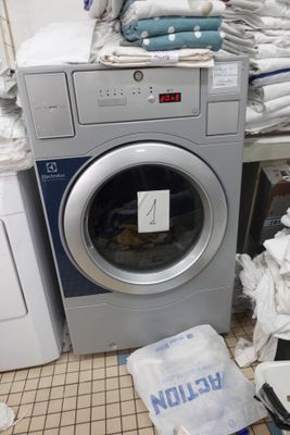 une machine à laver et un sèche-linge dans une pièce où il y a beaucoup de vêtements par terre