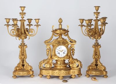 three gold colored candlesticks and a clock on a table