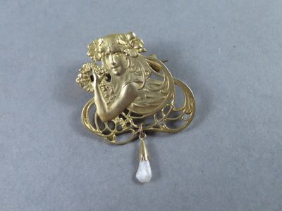 une image représentant une broche en or sur laquelle figure une femme tenant une perle