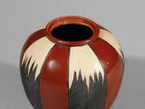 un vase rouge et noir posé sur une surface blanche
