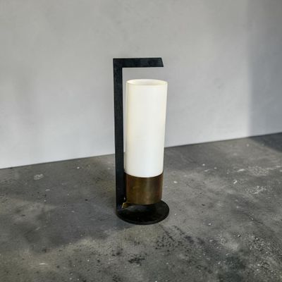 une bougie blanche posée sur un support noir, près d'un mur blanc