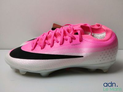 La chaussure de foot rose et noire se trouve sur une surface blanche.