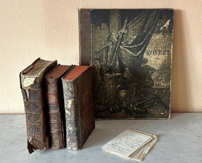 trois vieux livres posés sur une table à côté d'un tableau