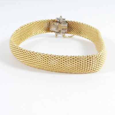 a close up of a gold mesh bracelet on a white background