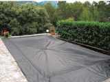 une bâche noire recouvrant une piscine dans un jardin