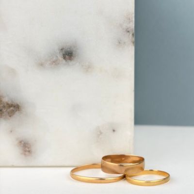 deux alliances en or posées à côté d'un bloc de marbre blanc