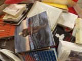 a pile of books on a bed with a red comforter