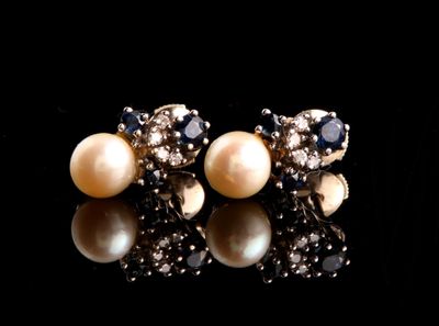 une paire de boucles d'oreilles en perles et diamants posées sur un fond noir
