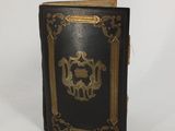 un vieux livre noir aux tranches dorées posé sur une surface blanche
