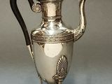 a silver tea pot with a black handle on a stand