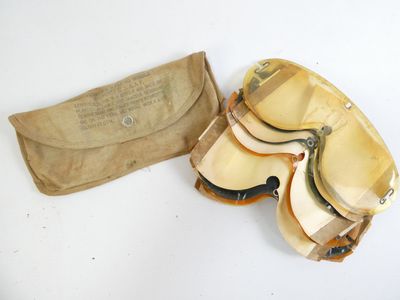 une vieille paire de lunettes de protection et une pochette posées sur une surface blanche