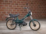 a small green motorcycle parked in front of a brick wall