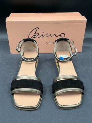 une paire de sandales noires et dorées avec un élément en forme de boîte sur le côté