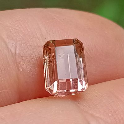 un diamant rose au doigt d'une personne, sur fond vert