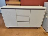 une armoire blanche à tiroirs, avec un réfrigérateur en arrière-plan