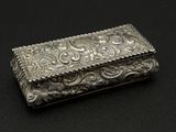 une boîte ancienne en argent posée sur une surface noire, avec un fond noir
