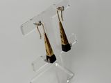 une paire de boucles d'oreilles dorées et noires posées sur un socle en acrylique transparent
