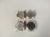 three watches are sitting on a white surface, one has a black face and one has a silver face