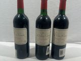 three bottles of red wine sit on a white surface next to each other