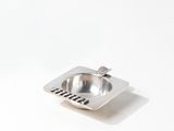 a metal ashtray on a white table with a spoon in it