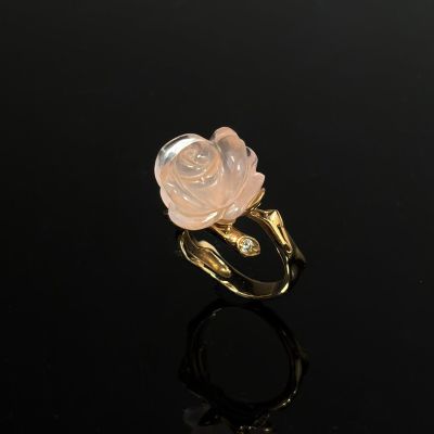 a gold ring with a pink rose on a black surface
