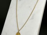 un collier en or orné d'une pièce de monnaie, posé sur une surface en marbre blanc