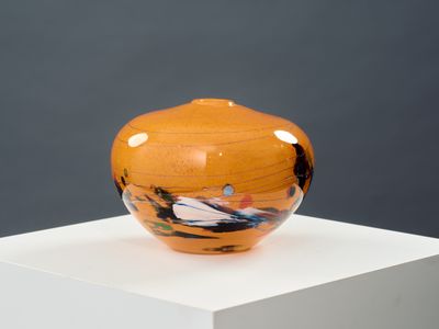 un vase orange posé sur un socle blanc