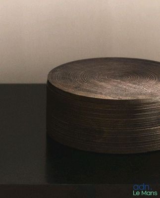un bol en bois posé sur une table noire, avec un mur blanc en arrière-plan
