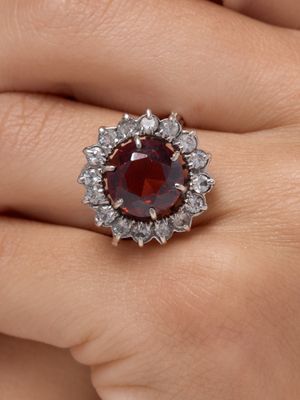 une image représentant la main d'une femme tenant une bague ornée d'une pierre rouge entourée de diamants blancs