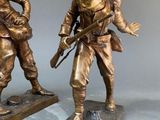 pair of bronze figurines of two men with guns and hats