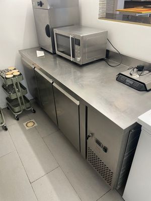 plan de travail en acier inoxydable dans une cuisine professionnelle équipée d'un micro-ondes et d'un réfrigérateur